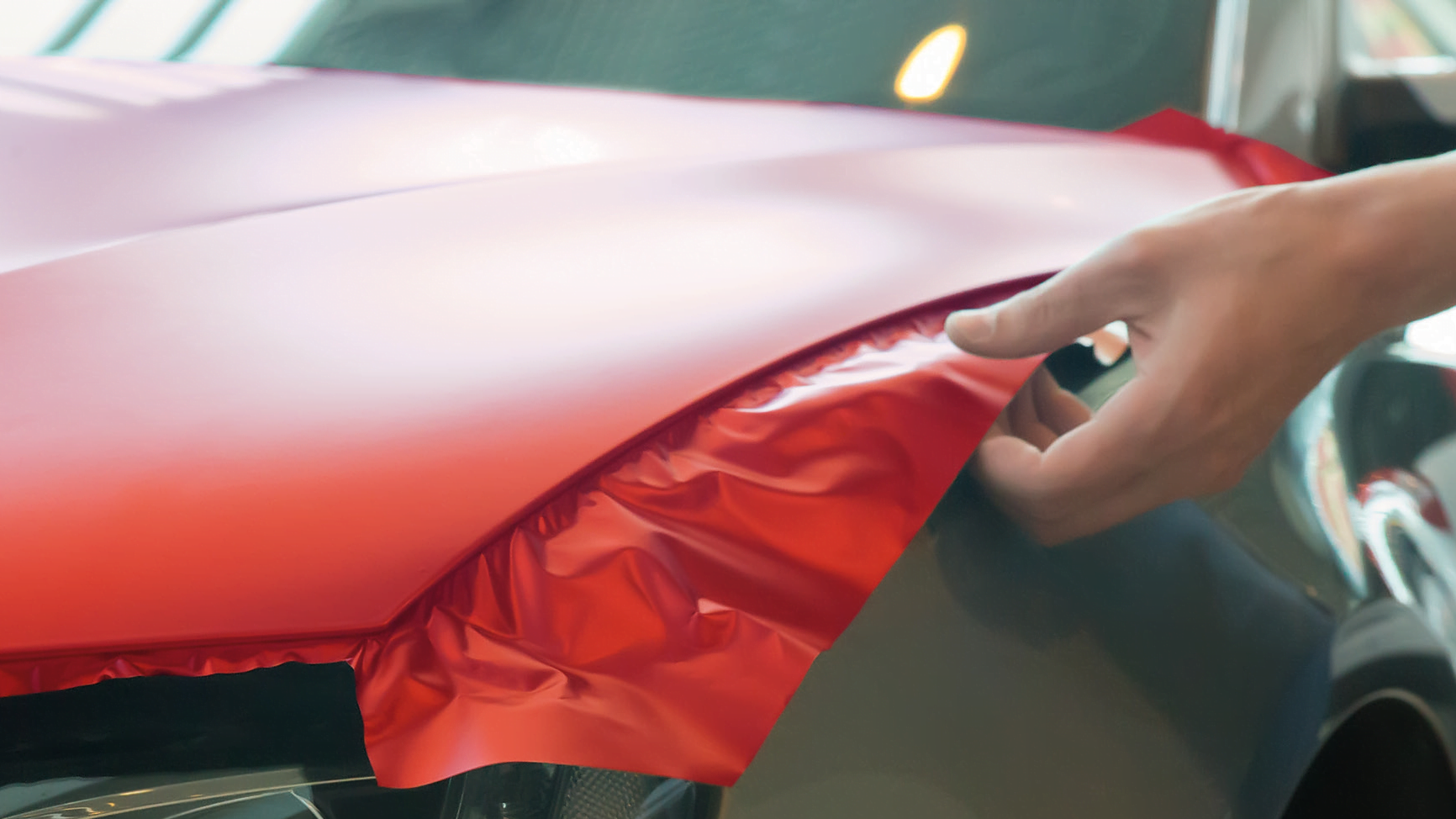 Detailaufnahme eines Karrosserieteils, das gerade mit einer roten Folie bezogen wird.